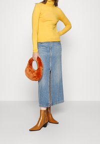 Maglione turtleneck giallo, gonna midi in denim con spacco frontale, borsa fluffy arancione e stivaletti marroni con punta e tacco basso.