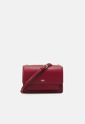 Sac bandoulière en cuir rouge foncé DKNY avec sangle ajustable et détail chaîne dorée sur fond blanc.
