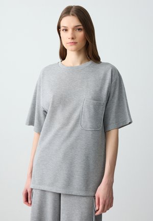 T-shirt gris surdimensionné en tissu doux, doté de manches courtes et d'une poche sur la poitrine. Le design est décontracté avec un col rond.
