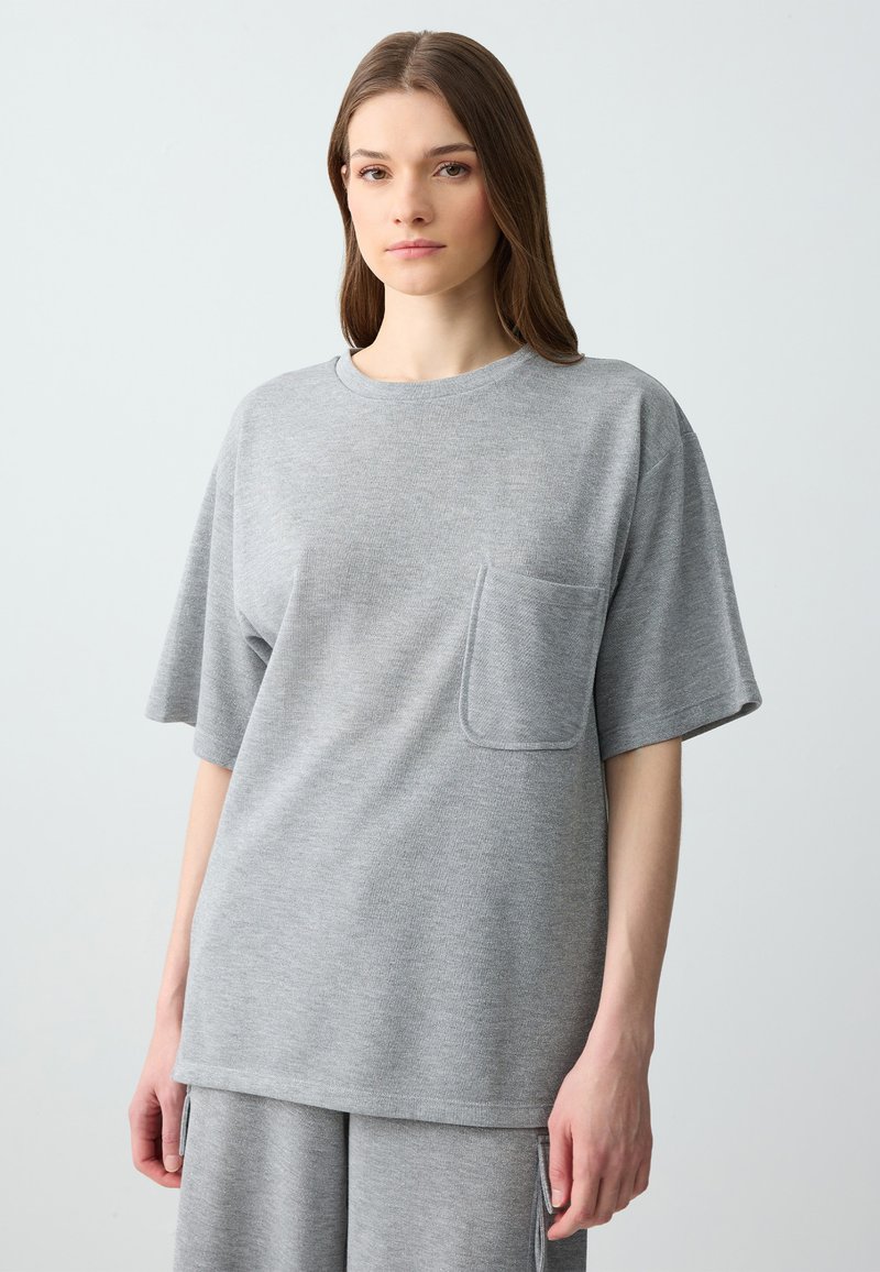 T-shirt gris surdimensionné en tissu doux, doté de manches courtes et d'une poche sur la poitrine. Le design est décontracté avec un col rond.