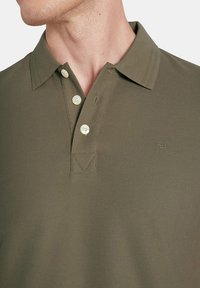 Oliwkowa koszulka polo wykonana z teksturowanej tkaniny, z trzema guzikami w zapięciu i małym logo na piersi.