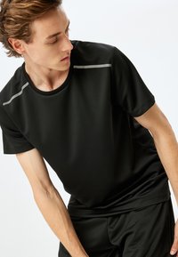 Czarny sportowy t-shirt wykonany z oddychającego materiału. Posiada krótkie rękawy, okrągły dekolt oraz odblaskowe akcenty na ramionach.