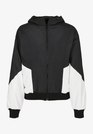 Sort og hvid hættebomberjakke med lynlås, elastiske manchetter og et karakteristisk trekantet farveblokdesign. Letvægtsmateriale.