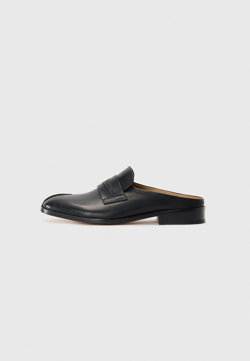 Svart läder slip-on sko med rund tå, låg blockklack och ett framrem. Slät textur med subtil logotypdetalj på remmen.
