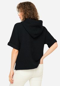 Felpa nera imbottita con maniche arrotolate e tasca frontale. Cappuccio sul retro, caratterizzato da un motivo testurizzato e design a vestibilità ampia.