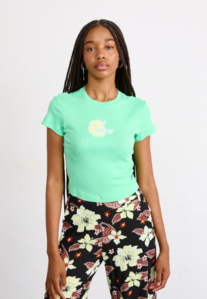 Mint green fitted t-shirt with a round neckline and short sleeves featuring a floral graphic. Worn with black floral patterned pants.
