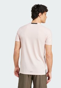 T-shirt rose clair à manches courtes avec un col rond, accent noir à l'arrière et petit logo à l'ourlet. Texture lisse, coupe décontractée.