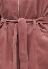 Ροζ τζιν μπουφάν με φερμουάρ μπροστά και δεμένη υφασμάτινη ζώνη στη μέση, με θηλιές για ζώνη και ορατές ραφές.