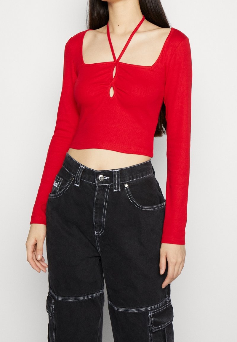 Kvinde iført en rød langærmet crop top med halterneck og nøglehulsudskæringer, parret med højtaljede sorte cargo-bukser med hvid syning.