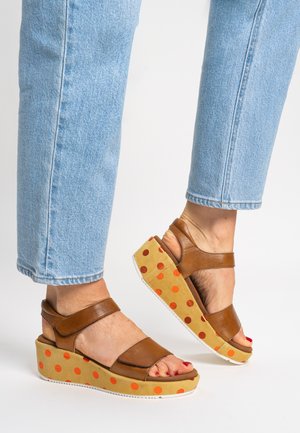 Brown leather sandals with two straps, a polka dot-patterned wedge sole in tan with orange dots, and a white rubber outsole.