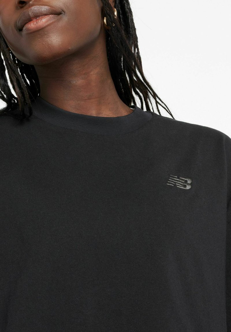 Black cotton t-shirt with a round neckline and short sleeves. Features a textured gray logo on the left chest area. Smooth fabric texture.