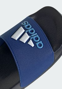 Sandalia tipo slide de Adidas con una tira texturizada azul, logo blanco y suela negra. El diseño es abierto en la parte delantera y cuenta con una plantilla acolchada.