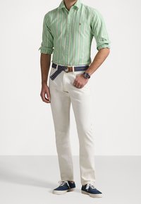 Camisa de manga larga a rayas verdes combinada con pantalones color crema, con un cinturón de rayas multicolores y zapatillas de deporte en color marino.