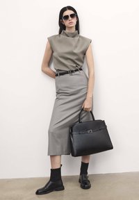 Graues ärmelloses Oberteil mit hohem Kragen, grauer Bleistiftrock, schwarzer Gürtel, schwarze strukturierte Handtasche und schwarze Ankle Boots mit dicken Sohlen.