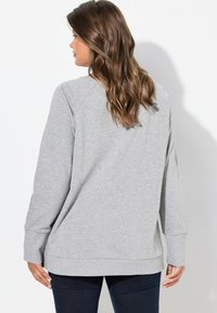 Sudadera gris con mangas raglán, tela texturizada, puños de canalé y un corte holgado, combinada con jeans oscuros para un look casual.