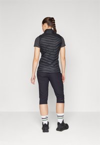 Colete puffer preto com um design em ziguezague, combinado com calças escuras e cropped. O modelo usa meias listradas brancas e verdes e ténis pretos.