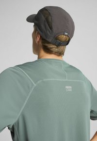 Roheline soonikkanga sportlik särk peegeldava logoga, koos tume mütsiga, millel on võrgusilma paneelid ja taga reguleeritav rihm.