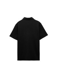 Polo shirt nero realizzato in tessuto testurizzato, con maniche corte, colletto classico e vestibilità rilassata. Nessun logo o motivo visibile.