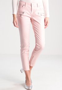 Rosa tajta byxor med en slät textur, fickor fram med dragkedja och dragkedjor vid anklarna. Matchade med metalliska silverskor för kontrast.