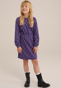 Lila klänning med diamantmönster, lång ärm, åtsittande i midjan. Matchad med svarta ankelstövlar och vita strumpor. Slät textur.