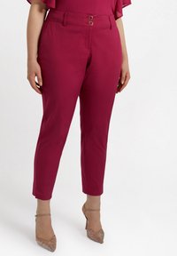 Pantaloni tapered fucsia cu o textură netedă, două butoane frontale și un brâu de talie medie, asortați cu pantofi cu toc transparent.