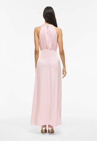 Šviesiai rožinė pastelinių atspalvių satino ilga suknelė su halterio kaklu ir iškirptės detalė nugaroje, aptempta juosmeniu ir laisvai krentančia sijono dalimi, derinama su metaliniais aukštakulniais.
