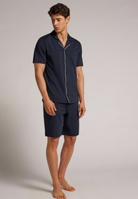 El conjunto de pijama de manga corta en color azul marino cuenta con una camisa con botones y detalles en blanco, acompañada de pantalones cortos a juego, fabricados con un tejido ligero.