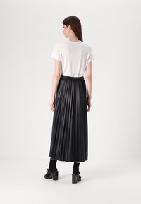 Jupe plissée noire avec une taille ajustée, associée à un t-shirt blanc. Modèle portant des sandales à talons et des chaussettes noires, vue de dos.