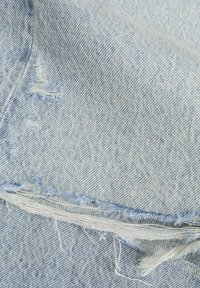 Vaaleansininen farkkukangas, jossa on rispaantunut reuna ja pieniä kuluneita reikiä, jotka paljastavat valkoiset langat alla.