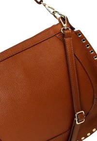 Braune Leder-Schultertasche mit strukturierter Oberfläche, verstellbarem Tragegurt und goldfarbener Hardware. Enthält Nietenakzente entlang des Randes.