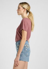 Top rosa a maniche corte abbinato a shorts in denim blu chiaro con ricami floreali e orlo frangiato.