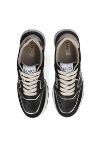 Baskets de sport noires avec une texture lisse, des lacets beiges contrastants, un col rembourré et des accents de design subtils. Logo visible sur la languette.