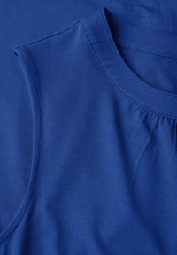 Tessuto di cotone blu con due porzioni superiori: una con scollatura a girocollo classica e l'altra con dettagli arricciati vicino allo scollo.