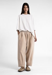 T-shirt en coton blanc surdimensionné avec des épaules tombantes, associé à un pantalon beige ample doté d'une taille élastique et d'un cordon de serrage, complété par des chaussures beiges.