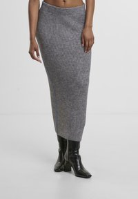 Gestrickter grauer Midirock mit geripptem Muster, versehen mit einer seitlichen Akzentuierung aus blauer Naht. Kombiniert mit schwarzen High-Heels.