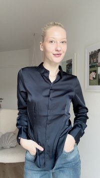 Must mustaga pikkade varrukatega särk, millel on nööpide ja krae, käed taskutes, neutraalse tausta taustal.