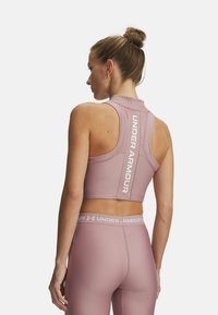 Roze sportieve cropped top met een hoge halslijn, een ruguitsparing en "UNDER ARMOUR" branding. Gladde textuur en aansluitende pasvorm.