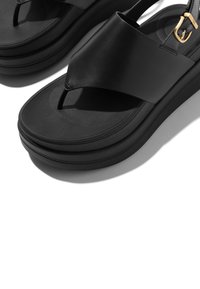 Sandales en cuir noir avec une tige en forme de lanière, une large bande et un détail de boucle dorée. Dotées d'une semelle plateforme épaisse et texturée pour plus de hauteur.