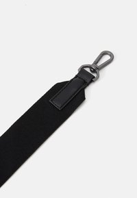 Sangle en toile noire avec des accents en cuir et un clip métallique. Caractéristiques d'une surface texturée et d'un design épuré et simple.