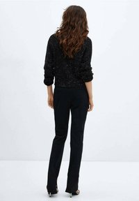 Czarny sweter o teksturowanej powierzchni z błyszczącymi detalami, w połączeniu z dopasowanymi czarnymi spodniami i sandałami na wysokim obcasie, widok z tyłu.