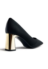 Zapato de tacón negro con un upper texturizado. Presenta un tacón de bloque metálico dorado, puntera afilada y forro negro liso.