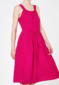 Vestido sin mangas de color rosa brillante con escote fruncido, cintura ajustada y falda acampanada. Hecho de una tela ligera, de textura suave.