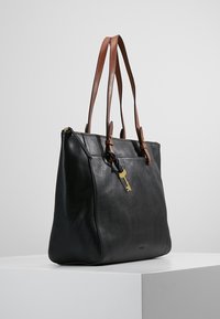 Zwarte leren totebag met twee bruine leren hengsels, een gouden sleutelsymbool en een gladde textuur; heeft een gestructureerde vorm en een ritssluiting.