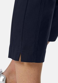 Marineblaue, verkürzte Hosen aus leichtem Material. Auffälliges Schlitzdetail am Saum, mit sauberer Naht und glatter Textur.