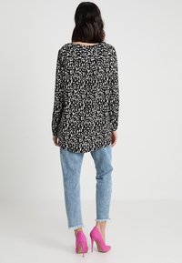 Černobílé tričko s leopardím potiskem s dlouhým rukávem, v kombinaci se světle modrými džínami s efektem opotřebení a jasně růžovými lodičkami na vysokém podpatku.