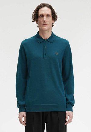 Polo a maniche lunghe di colore teal realizzato in tessuto testurizzato, dotato di una pattina con tre bottoni e un piccolo logo ricamato sul lato sinistro del petto.