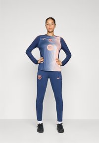 Ensemble de sport de la Marine comprenant un haut à manches longues avec un design dégradé, un logo Nike et un écusson du FC Barcelone ; pantalon ajusté assorti avec des accents de logo.