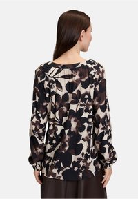 Floral blouse in black, cream, and brown tones. Features long sleeves, a scoop neckline, and gathered detailing at the back.