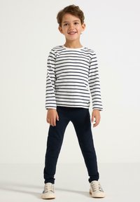 Stribet langærmet skjorte i hvid og navy, parret med navy leggings og lyse sneakers. Behageligt, tætsiddende design med blød tekstur.