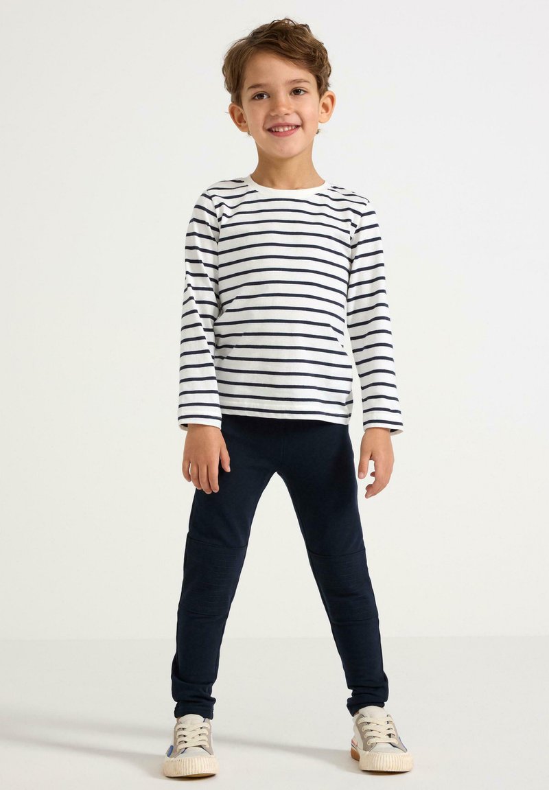 Stribet langærmet skjorte i hvid og navy, parret med navy leggings og lyse sneakers. Behageligt, tætsiddende design med blød tekstur.